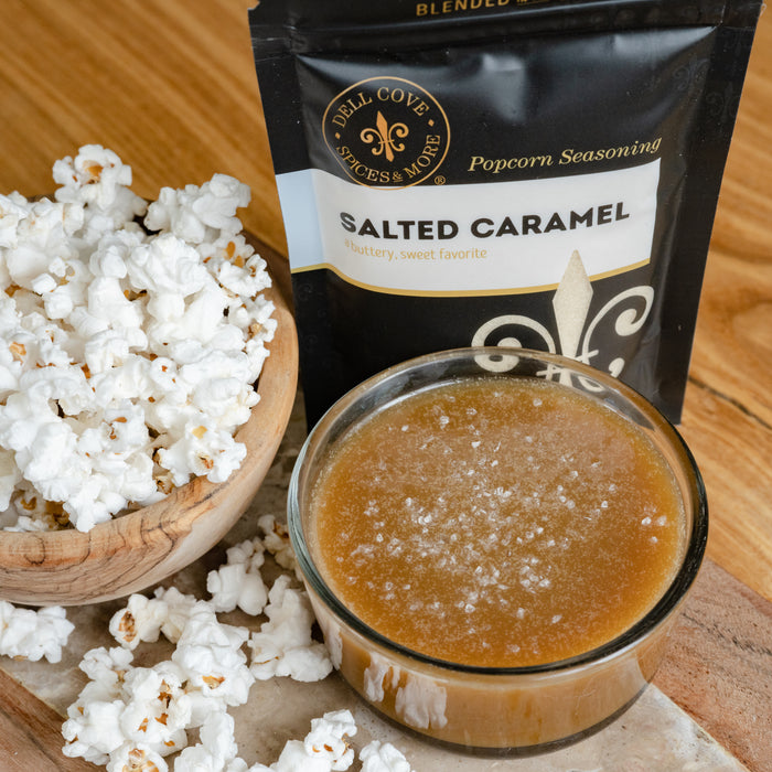 Small glass bowl filled with caramel sauce next to wooden bowl with popped popcorn and Salted Caramel seasoning pouch - Dell Cove Spices