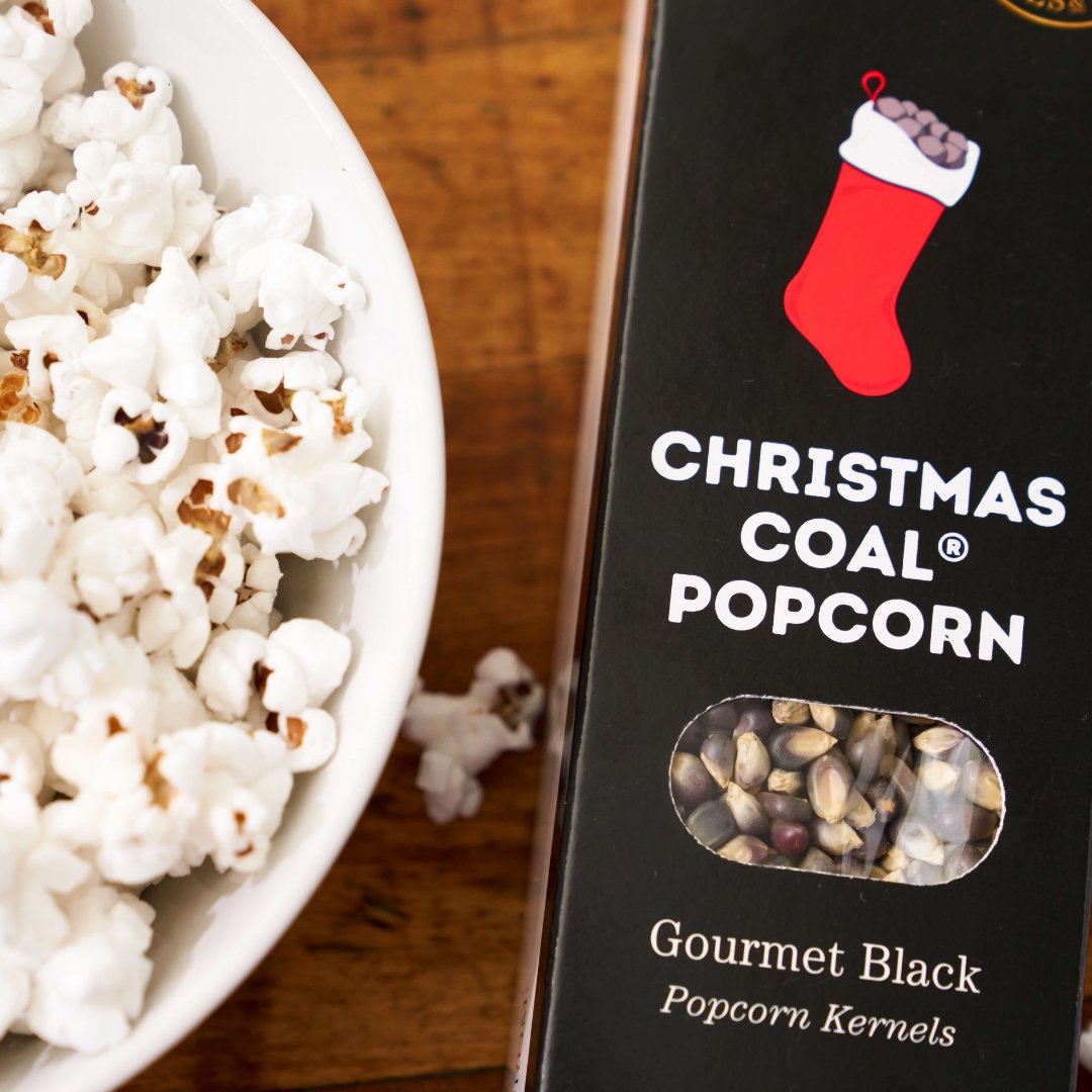 Box of Dell Cove Christmas Coal Popcorn next to a bowl of popcorn on a wooden surface - fun Christmas sock gift