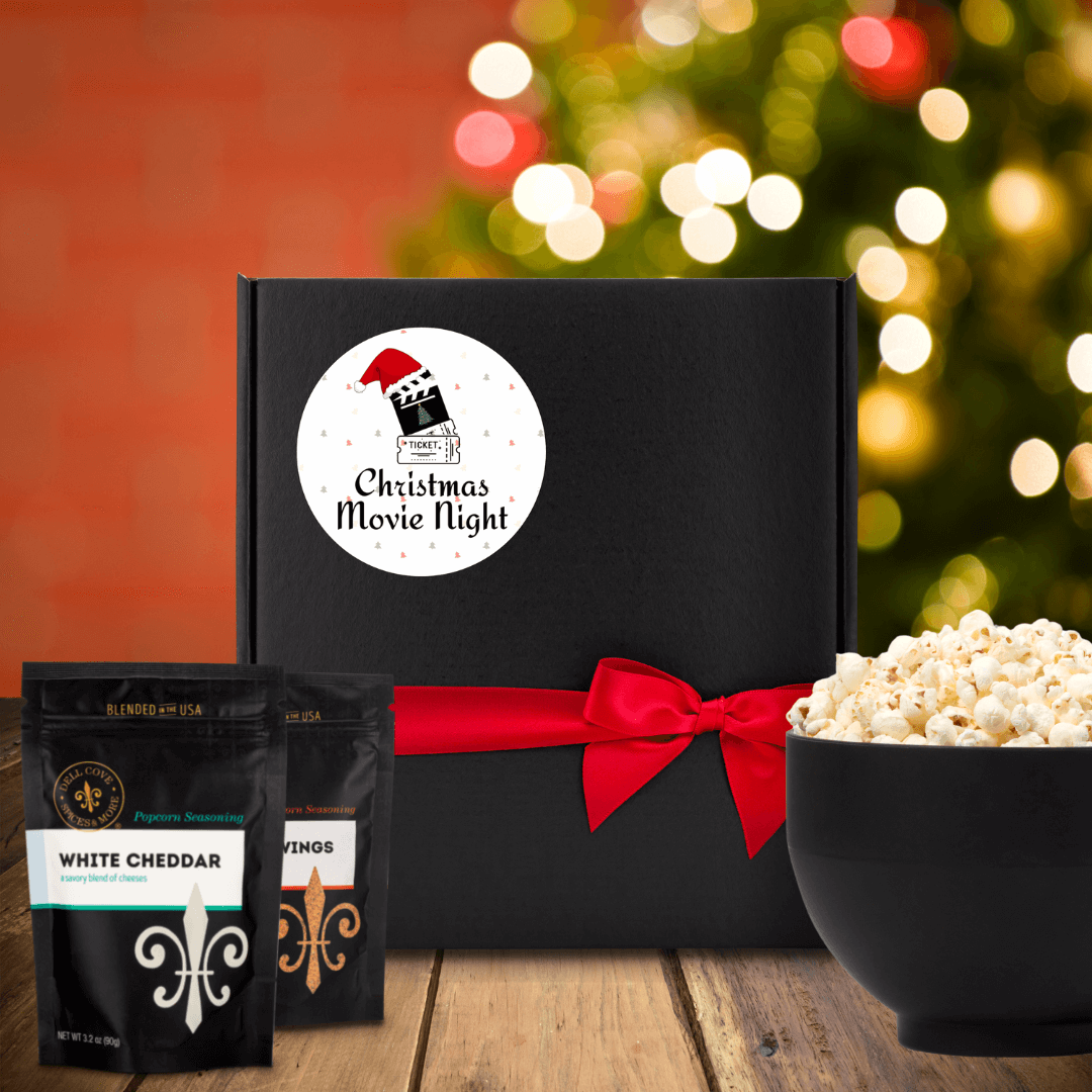 Black gift box with round white label. Label shows a red and green mini tree background with movie tickets, a film clapper with a Santa hat and the words Christmas Movie Night. Dell Cove Spices
