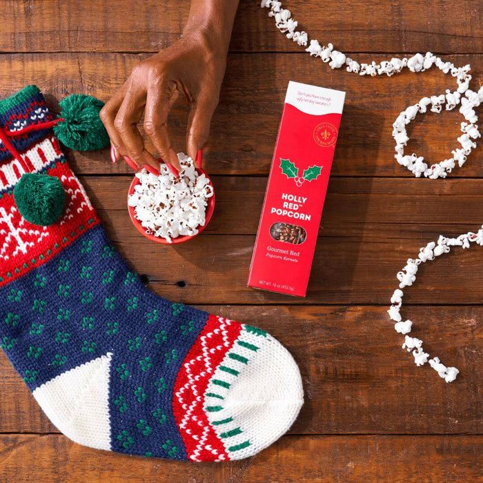 Christmas-themed Dell Cove® Holly Red popcorn kernels that pop fluffy and crunchy for Christmas snacking - with a Christmas sock on a wooden surface