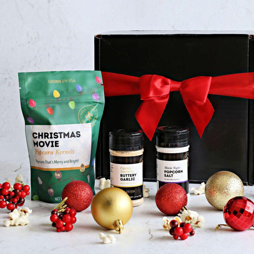 Dell Cove Spices gift box with Christmas-themed popcorn kernels and seasonings in a Christmas Movie Night Popcorn Kit, surrounded by festive ornaments on a light background.