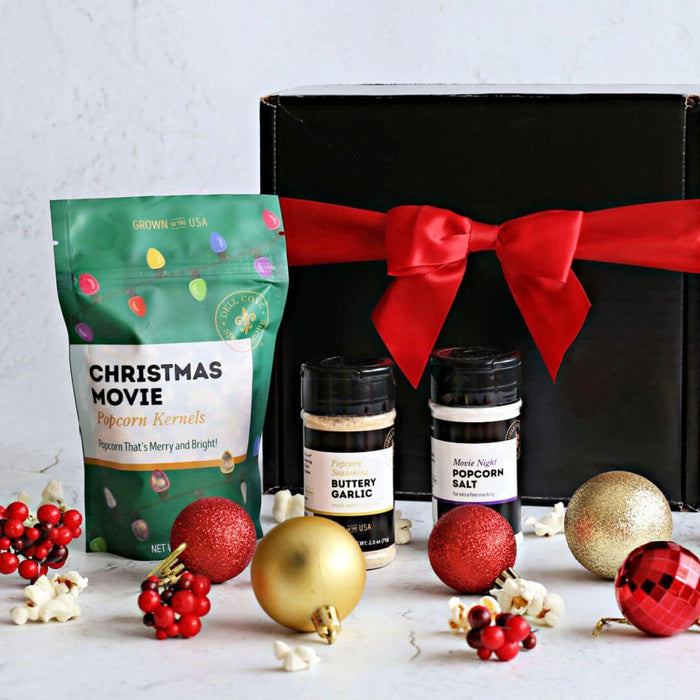 Dell Cove Spices gift box with Christmas-themed popcorn kernels and seasonings in a Christmas Movie Night Popcorn Kit, surrounded by festive ornaments on a light background.