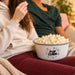 Two people enjoying freshly popped popcorn together on the couch during a cozy movie night at home.