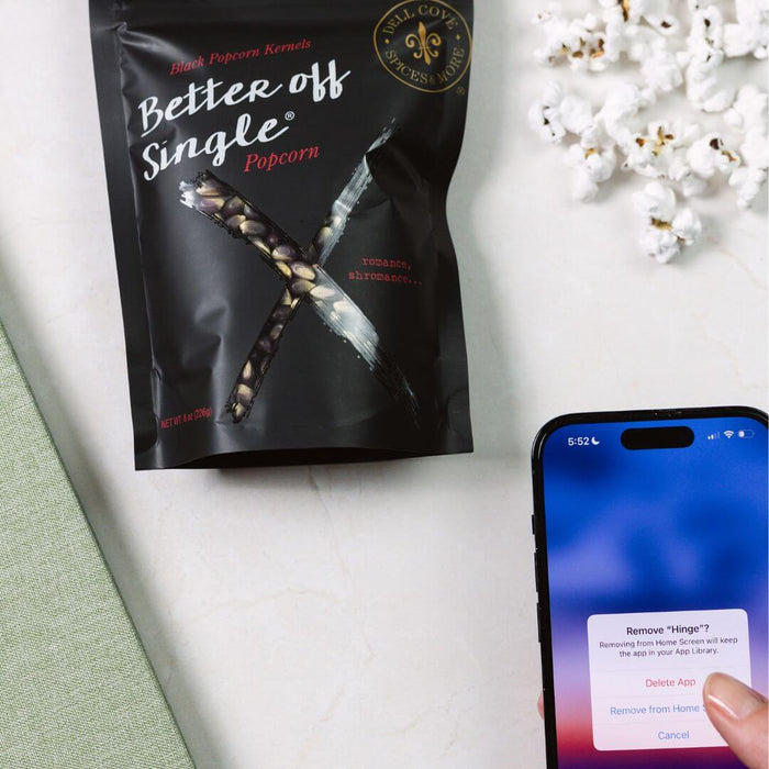 Woman deleting the Hinge app while snacking on Dell Cove Better Off Single popcorn – funny breakup gift
