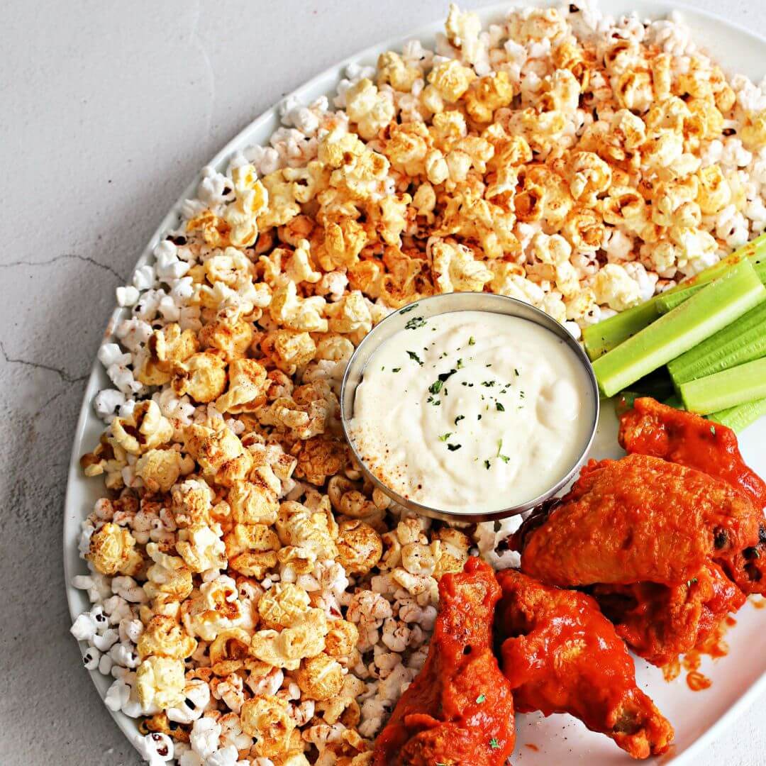 Buffalo popcorn with Dell Cove® seasoning, crispy wings, celery, and blue cheese dip on a game day snack board.