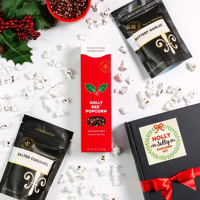 Popcorn packages and a box labeled 'Holly Jolly Popcorn Kit' on a white surface with popcorn kernels.