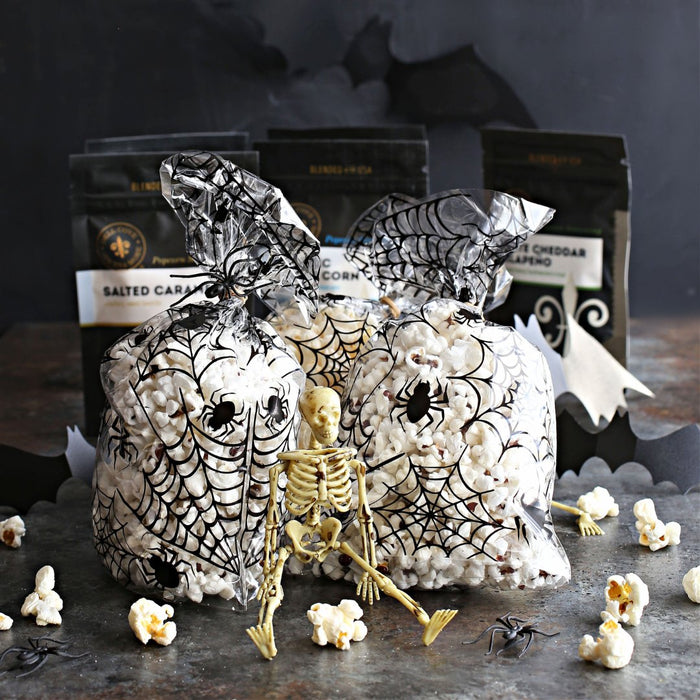 Halloween-themed popcorn bags with spider webs and a skeleton figure on a dark surface.