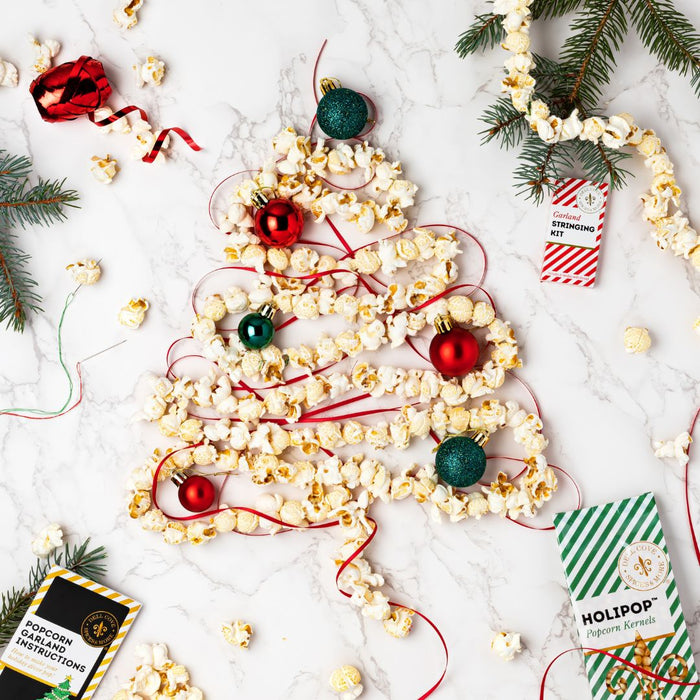 Popcorn arranged in the shape of a Christmas tree with decorative ornaments and a popcorn garland kit on a white surface.