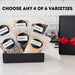 Six varieties of Dell Cove gourmet popcorn kernels displayed in resealable pouches beside a black gift box with red satin ribbon. Choose any four varieties.
