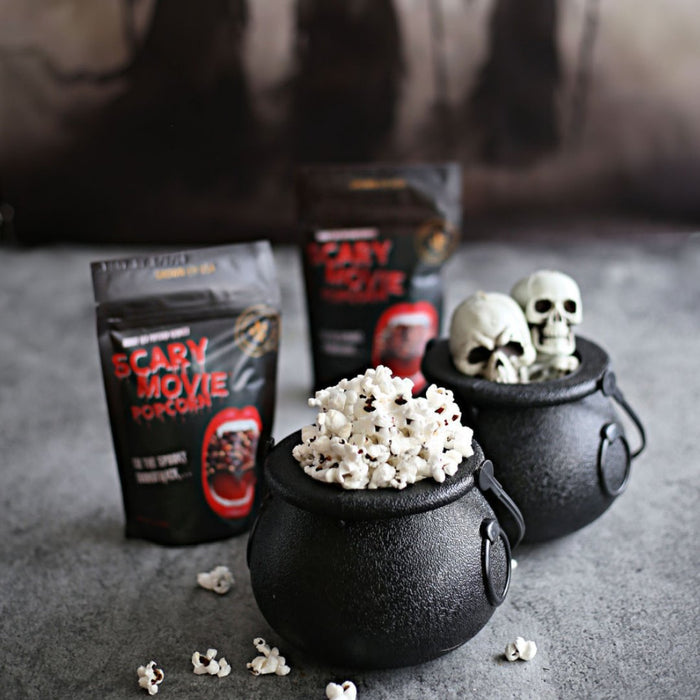 Popcorn in black cauldrons with 'Scary Movie Popcorn' packages on a gray surface.