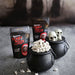 Popcorn in black cauldrons with 'Scary Movie Popcorn' packages on a gray surface.