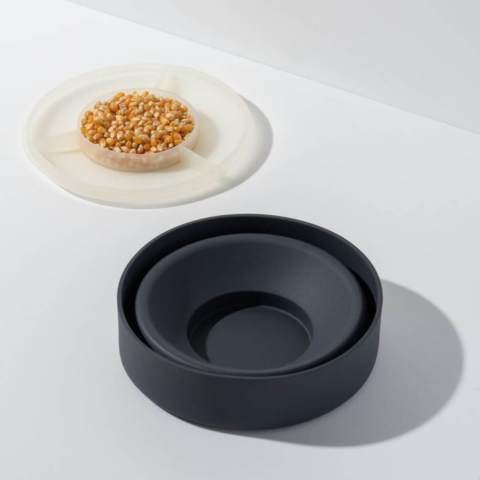 Collapsible black silicone microwave popcorn popper with measuring lid filled with loose popcorn kernels