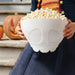 Person holding a white skull-shaped bowl filled with popcorn, with pumpkins in the background.