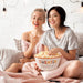 Two young women sharing a Sweater Weather fall colored enamel popcorn bowl bucket filled with popped popcorn 