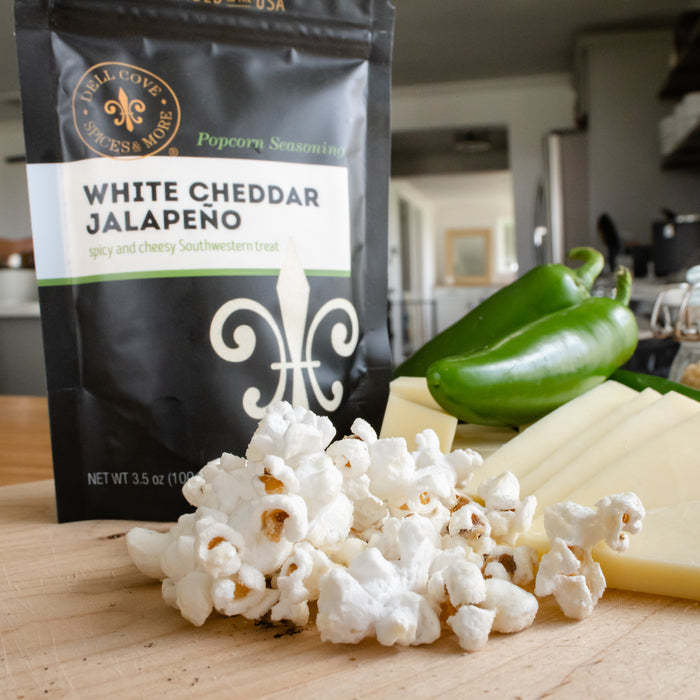 Small pile of popped popcorn on table with blocks of cheddar cheese, jalapenos and White Cheddar Jalapeno seasoning pouch behind - Dell Cove Spices
