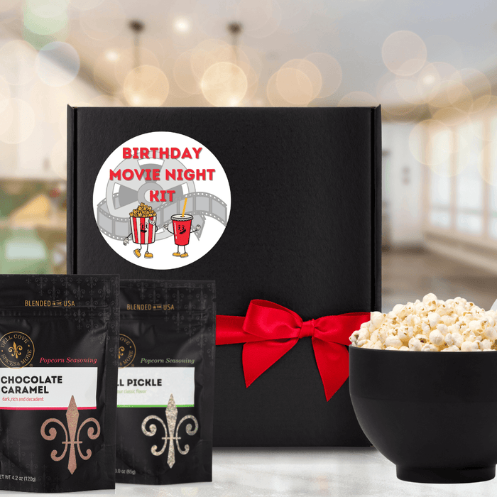 Black gift box featuring round label with old fashioned film and popcorn and soda characters with text Birthday Movie Night Kit next to large black bowl filled with popped popcorn and two seasoning pouches - Dell Cove Spices