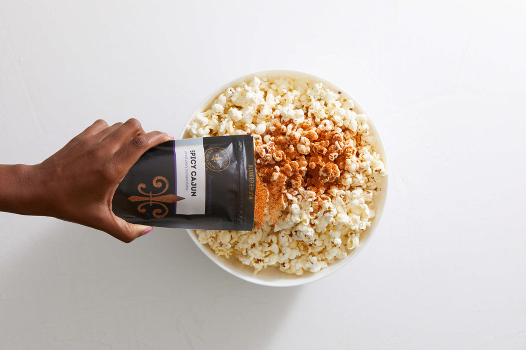 Hand sprinkling Spicy Cajun popcorn seasoning from pouch on to large bowl of popped popcorn - Dell Cove Spices