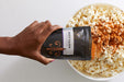 Hand sprinkling Spicy Cajun popcorn seasoning from pouch on to large bowl of popped popcorn - Dell Cove Spices